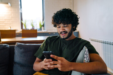 Young indian handsome man sitting on sofa with phone
