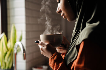 Young calm woman in hijab holding cup of hot tea - obrazy, fototapety, plakaty