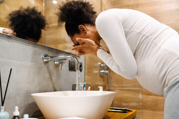 Young beautiful pregnant afro woman washing her face