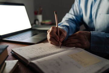 Man hands taking notes in notebook next to laptop closeup