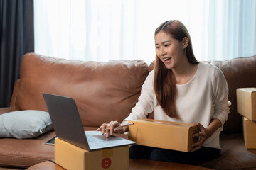 Asian female online store small business owner entrepreneur seller packing box checking website retail order using laptop preparing delivery parcel on table. Dropshipping concept. Closeup