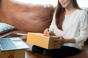 Asian female online store small business owner entrepreneur seller packing box checking website retail order using laptop preparing delivery parcel on table. Dropshipping concept. Closeup