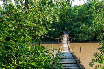 Suspended wooden bridge to the other side of the river. Suspension bridge in a small village