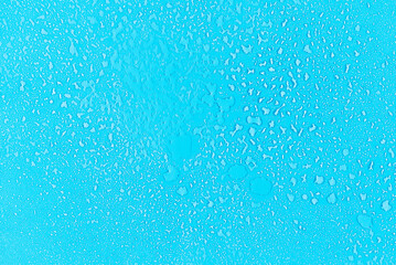 Water drops condensate on blue background texture on transparent glass. backdrop glass covered with abstract drops of water.