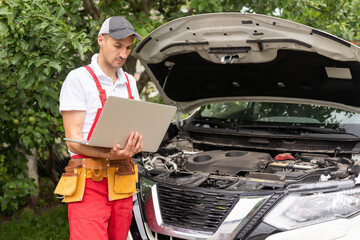 Mechanic with laptop near car engine. Modern car diagnostic program on screen. Car service concept