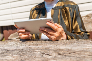 Senior woman making video call from pc tablet computer outside in summer day.
