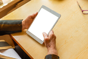 Senior woman hands holding and using pc tablet empty white screen mockup while sitting at the table...