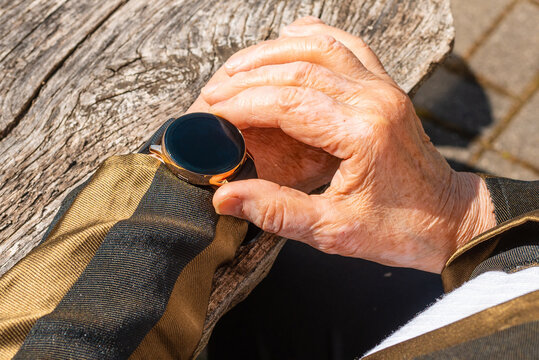 Elderly Woman With Smart Watch Fitness Band Checking Her Pulse,outdoors On The Old Wooden Table,sumer Sunny Day. Closeup.