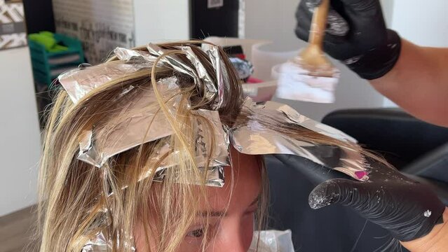 Putting hair dye on the strand of hair. Colouring hair at beauty salon. 4K.