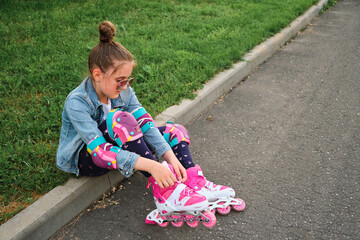 Pretty little girl learning to roller skate on beautiful summer day in a park.