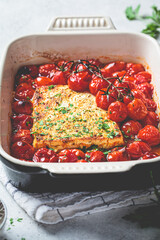 Baked feta cheese with tomatoes in dish. Trendy homemade recipe.