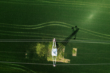 Transmission tower supporting overhead power line through cultivated crops field, aerial view from...