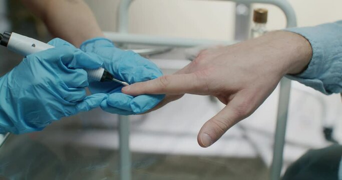 Manicurist master woman is doing hardware manicure to man, hands closeup.