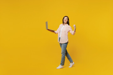Full body young happy smiling woman she 30s wear striped shirt white t-shirt hold use work on laptop pc computer do winner gesture isolated on plain yellow background studio. People lifestyle concept