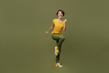 Fototapeta na wymiar Full body young excited happy woman she 20s wear yellow t-shirt doing winner gesture celebrate clenching fists say yes isolated on plain olive green khaki background studio. People lifestyle concept.