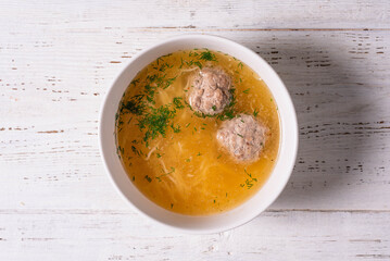 soup with noodles and meatballs on a white wooden background