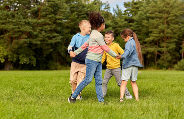 Naklejka na ściany i meble childhood, leisure and people concept - group of happy kids playing round dance at park