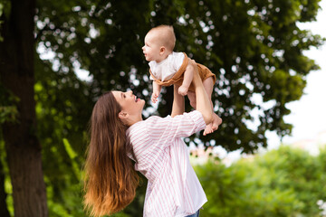 Photo of excited cheerful mother little son dressed casual clothes rising arms enjoying sunshine outdoors backyard