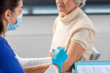 medicine, health and vaccination concept - close up of doctor or nurse with syringe making vaccine or drug injection to senior woman in mask at hospital