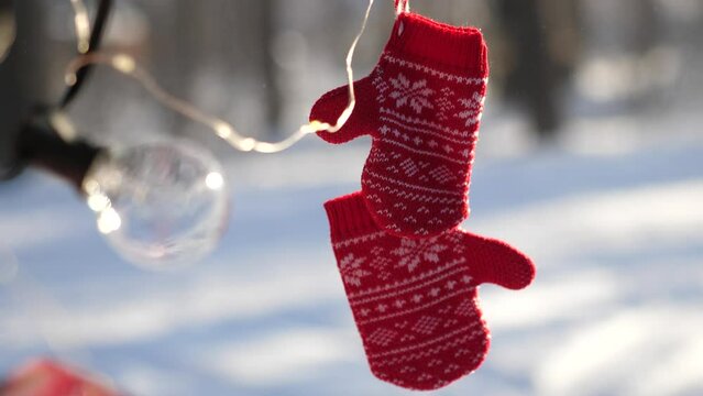 Red wool gloves with a pattern and garland hanging on a leash. Wintertime, winter forest concept. Red mittens hanging on a branch in winter forest. Selective focus.
