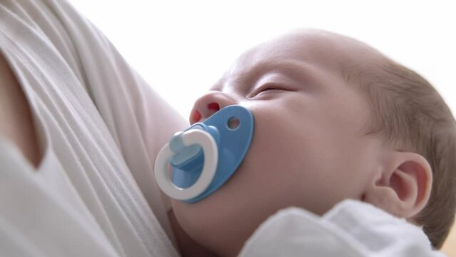 Little newborn baby boy sleeping with baby dummy on mother hands at home, Mom puts baby to sleep during the day