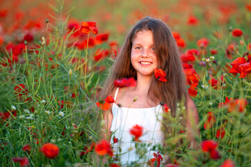 Naklejka premium cute girl wearing white dress in summer blooming poppy field walking under evening sun