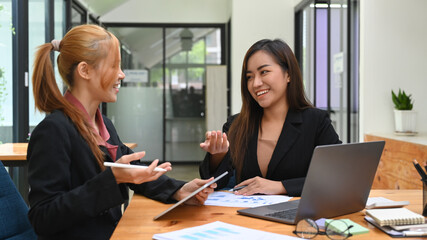 Two happy business colleagues discussing business project, working together in office