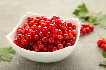 Bowl with ripe red currant on grey background.