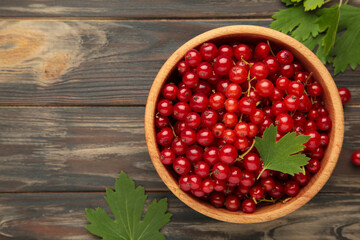 Bowl with ripe red currant on brown wooden background. Top view.