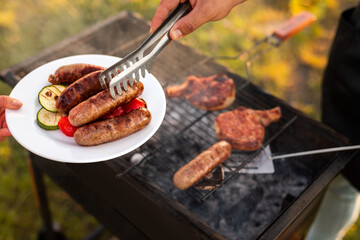 Crop chef serving sausages and vegetables during picnic