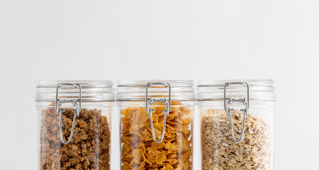 food storage, healthy eating and diet concept - close up of jars with oat, corn flakes and granola on white background