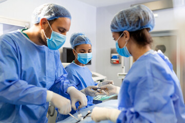 Surgical Team Working In Operating Theatre Wearing Protective Clothing