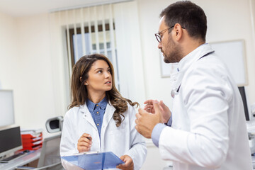 Doctors discussing over a medical report in hospital. Female and male doctor checking clinical report of patient online. Healthcare staff having discussion in a office of private clinic.