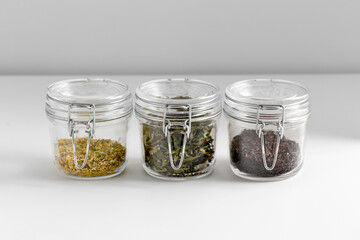 healthy eating and storage concept - jars with dried herbs on white table