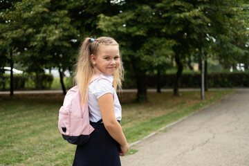 happy blonde curly schoolgirl in school uniform with pink backpack back to school outdoor
