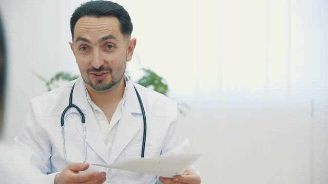 4k video of doctor wearing white lab coat holding ultrasound photos and explaining.