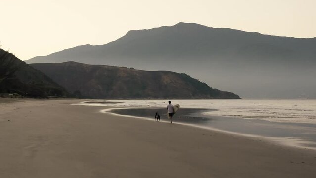 Surfer walking on the Beach with his Dog