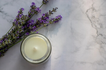 Obraz na płótnie Canvas Lavender flowers and aromatic white candle in a jar on white marble table background. Relaxing spa concept. Top view, flat lay, copy space