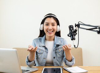 Content creator woman host streaming her a podcast on laptop with headphones and microphone...