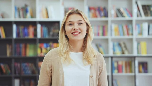 Female blogger influencer talking to camera, recording video or having conference call, bookshelves on blurred background. Girl giving interview online. Student making presentation in library