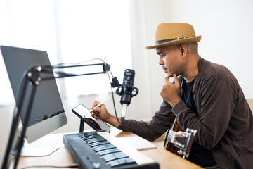 Professional Musician song writer with condenser microphone note on tablet. Hispanic male composing...