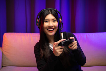 Playing video game. Young asian pretty woman with headphone sitting on sofa holding joystick in...