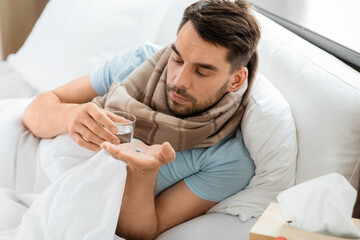 people and health problem concept - unhappy sick man with medicine pill and glass of water lying in bed at home