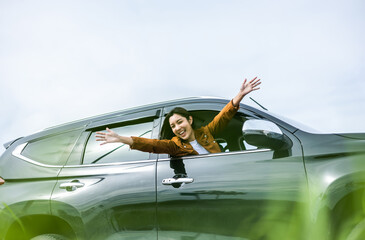 Young beautiful asian women getting new car. she very happy and excited. Smiling female driving vehicle on the road on a bright day. Sticking her head outta the windshield