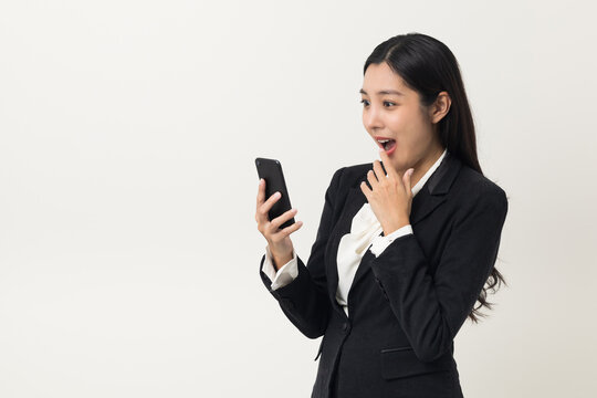 Happy young asian business woman using smartphone on isolated white background. Attractive female in suit holding cell phone feeling happy. Portrait shot in studio.