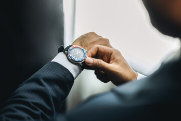 Confident businessman in classic blue suit wearing or adjust watch with necktie near window in...