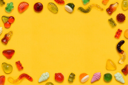 Gummy candy frame border, assorted jelly gum fruit candy sweets on yellow background top view flat lay