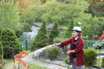 Garden care, hobbies and outdoor activities. A girl in a plaid shirt and hat is working in the garden - cutting bushes, watering and planting plants, smelling flowers at sunset. Summer leisure
