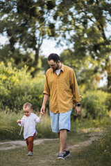 Fototapeta premium A father spends time with his son. Happy parenthood. A father and his son are walking in the field. The father is his toddler son.
