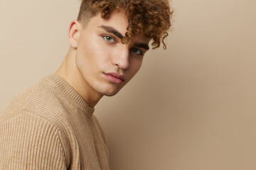 Fototapeta premium close horizontal portrait of a handsome, charming man with curly hair standing in a beige sweater on a beige background